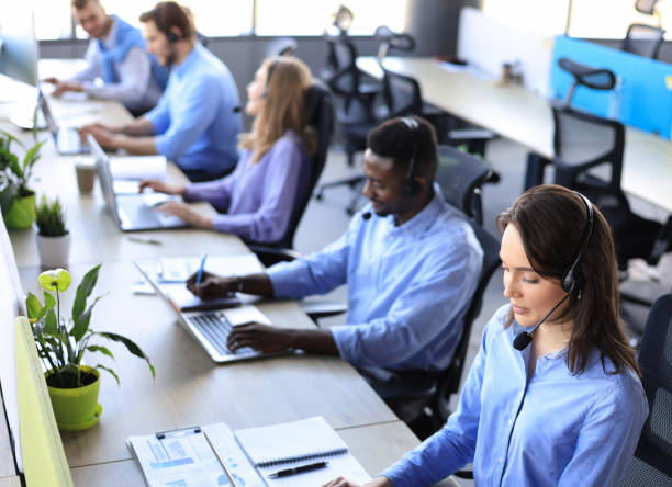 istock Female customer support operator with headset and smiling, with collegues at background. 1322087609