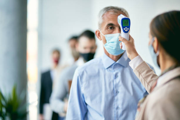 mature businessman getting his temperature measured at checkpoint of an office building. - infrared thermometer imagens e fotografias de stock