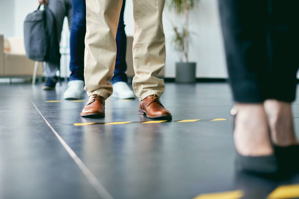 Close-up of business people standing in a row behind social distance lines. Close-up of businessman standing behind social distancing line while waiting with group of coworkers at office building hallway. people standing in line social distance stock pictures, royalty-free photos & images