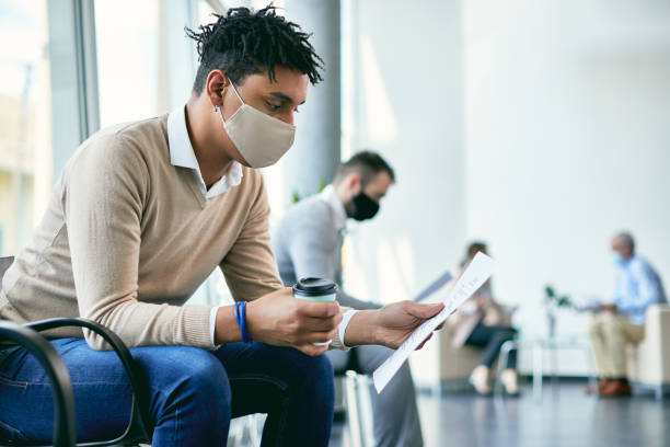African American candidate going through his resume while waiting for job interview during coronavirus pandemic. Young black businessman with face mask analyzing his CV while sitting in waiting room and preparing for job interview. candidate photos stock pictures, royalty-free photos & images