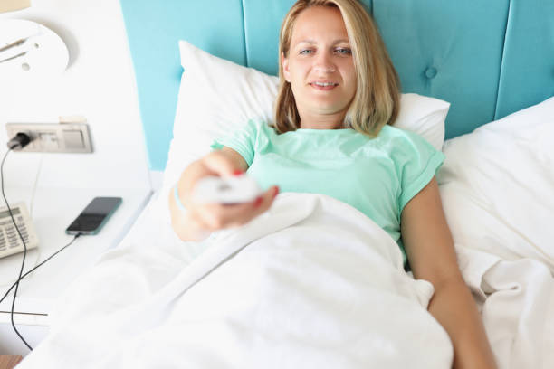 istock Young woman lying in bed with TV remote control in her hands 1322089082