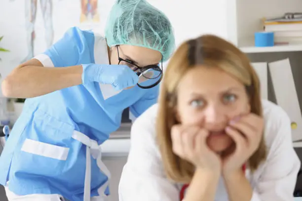 Doctor examining woman rectum with magnifying glass in clinic. Treatment of hemorrhoids after childbirth concept