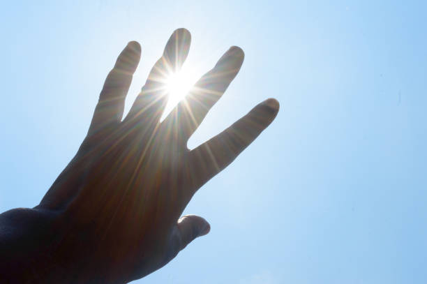 人間の手を通して注ぐ暑い夏の太陽光線。太陽の光の熱温度を覆う手。紫外線や日焼け背景からの保護。 日射病、熱中症、温室効果。 - 日焼け ストックフォトと画像