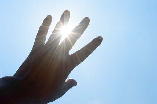 Hot summer sunlight rays pouring through human hand. Hand covering sun light heat temperature. Protection from ultraviolet light and sunburn background.  Sunstroke, heatstroke, greenhouse effect.