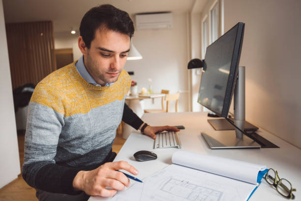 istock Architect sitting by the desk in his home office looking at blueprints 1322103508