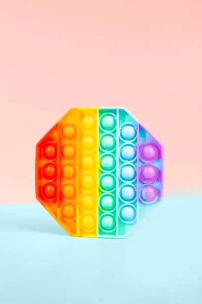 Photo of Pop it toy for children. rainbow octagon on pink and blue background. antistress toy