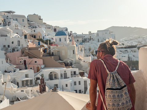 He looks at Oia town, people exploring Greece concept.