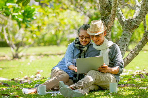 istock asian couple  sitting under the tree  at park  using  laptop 1322107354