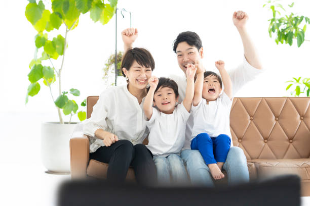 parents and children watching TV with their hands raised Image of parents and 2 boys watching TV with their hands raised asian kids watching tv stock pictures, royalty-free photos & images