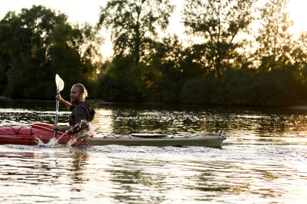 istock Young guy holding a paddle while boating on a lake surrounded by peaceful nature at sunset 1322113122