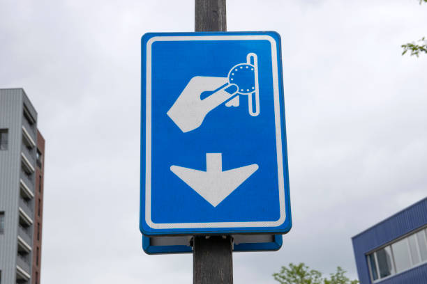 A blue and white road sign indicating the city of Rotterdam, mounted on a grey pole, viewed against a dark, sheltered background