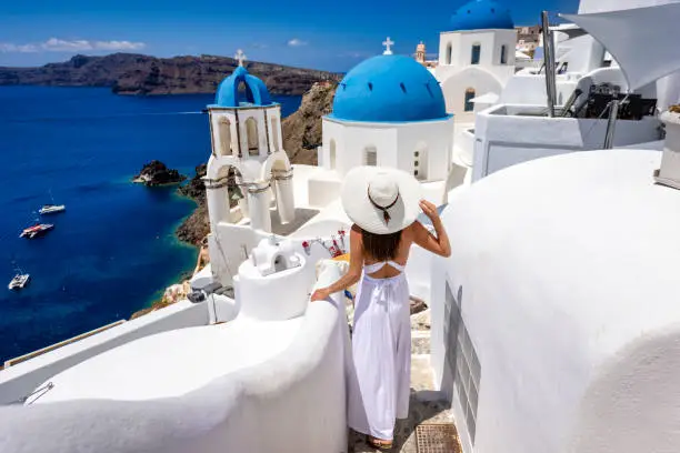 Photo of A tourist woman in a white dress explores the village of Oia on Santorini island