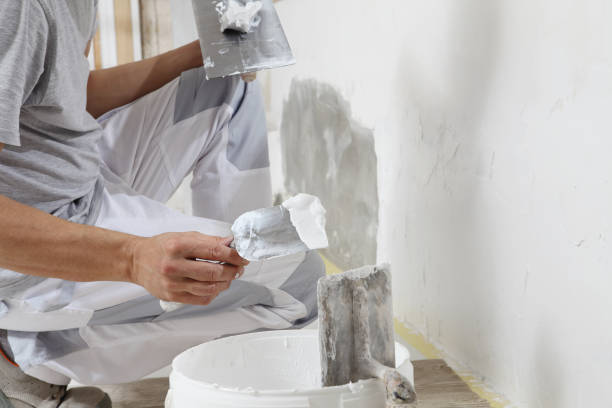 istock Hands man plasterer construction worker at work closeup, takes plaster from bucket and puts it on trowel to plaster the wall, inside the building site of a house 1322114836