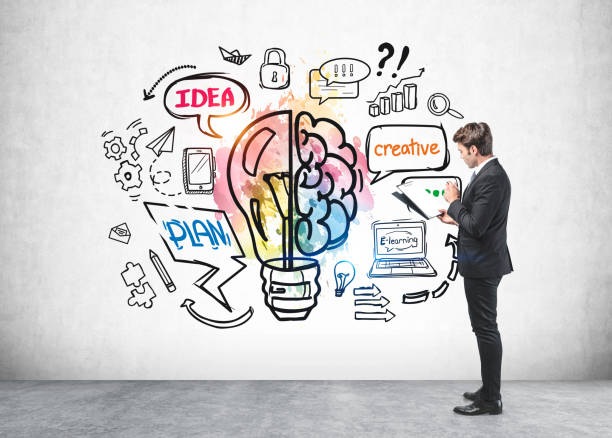 istock Side view of businessman in suit checking his notes in folder and standing in front of concrete wall with colorful lightbulb and brain sketch. Concept of success and future career opportunities. 1322114922