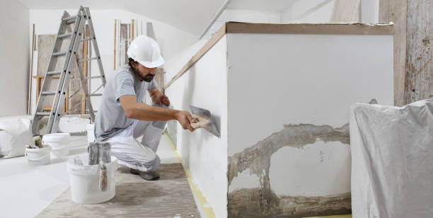 istock man plasterer construction worker at work, takes plaster from bucket and puts it on trowel to plastering the wall, wears helmet inside the building site of a house 1322114935