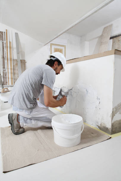 istock man plasterer construction worker at work, takes plaster from bucket and puts it on trowel to plastering the wall, wears helmet inside the building site of a house 1322115123