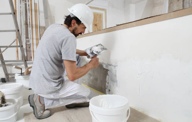 istock man plasterer construction worker at work, takes plaster from bucket and puts it on trowel to plastering the wall, wears helmet inside the building site of a house 1322115155
