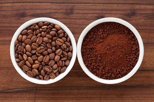 Two bowls containing roasted coffee beans and instant coffee