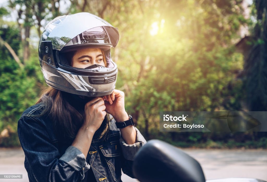 Confidence Asian woman wearing a motorcycle helmet before riding. Helmets contribute to motorcycle safety by protecting the rider's head. Motorcycle Stock Photo