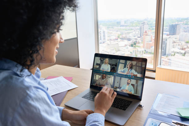 African American businesswoman having working video call in global office. Young happy African American businesswoman ceo having working videocall on financial report with multiethnic colleagues using laptop in modern corporation global office. Over shoulder view. financial advisor virtual stock pictures, royalty-free photos & images