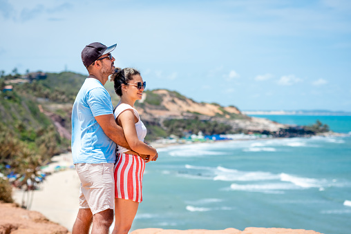 Smiling couple standing arm in arm together on a beach and looking out at the ocean view