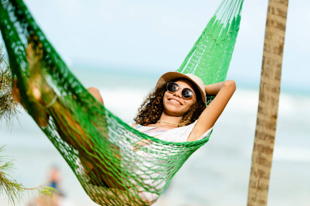 Young woman relaxing in a hammock at beach Young woman relaxing in a hammock, in a sunny day using sunglasses and a hat, at beach girls laying on beach stock pictures, royalty-free photos & images