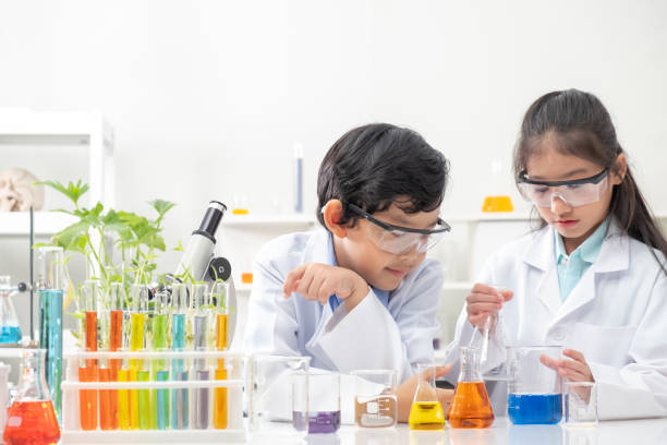 istock Young Asian boy and girl smile and having fun while doing science experiment in laboratory classroom with Teacher. Study with scientific equipment and tubes. Education concept. 1322144083