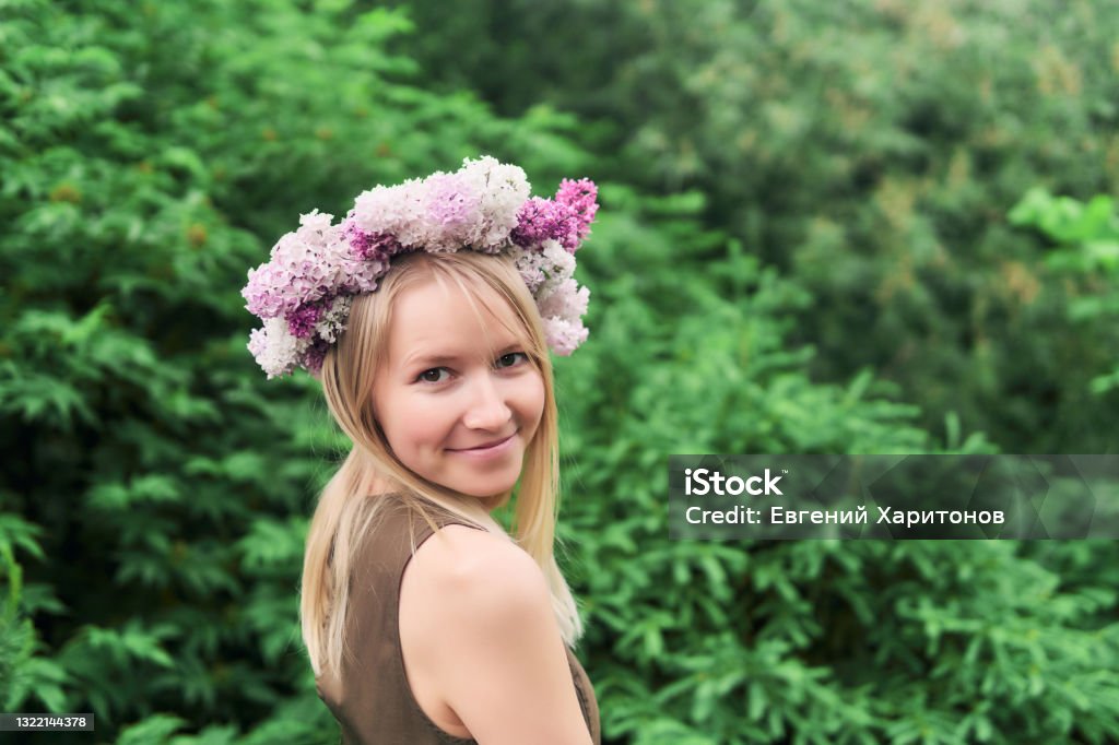 young woman in a floral wreath of lilac flowers on a natural background outdoors happy young woman in a floral chaplet of lilac flowers on a natural background outdoors Floral Crown Stock Photo