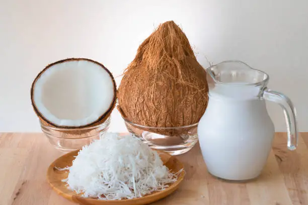 Coconut products, a whole coconut, halves, grated and coconut milk set on wooden table, white background and copy space.