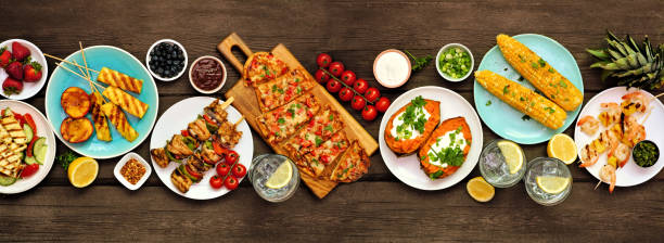 istock Summer BBQ grill table scene over a dark wood banner background. Above view. 1322150451