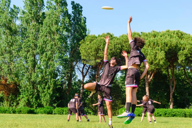 Group of young teenagers people in team wear playing a frisbee game in park oudoors. jumping man catch a frisbee to a teammate in an ultimate frisbee match. milennials friends outside in a garden Group of young teenagers people in team wear playing a frisbee game in park oudoors. jumping man catch a frisbee to a teammate in an ultimate frisbee match. milennials friends outside in a garden plastic disc stock pictures, royalty-free photos & images