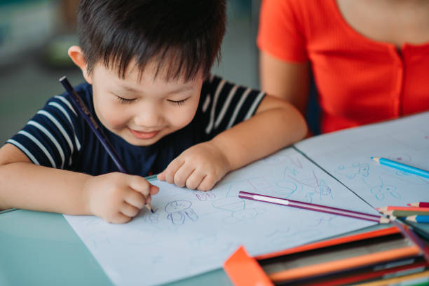 Asian chinese smiling cute little boy drawing with colour pencil in art class stock photo