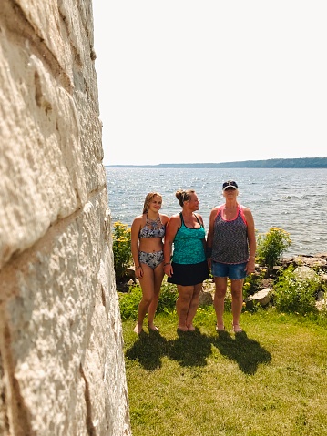 Three female family members, daughter, mother, and grandmother, standing outdoors near the lake shore and standing together showing three generations enjoying a day at the Lake. Partial view of lighthouse can be seen. Taken in Gladstone, Michigan in The Upper Peninsula.