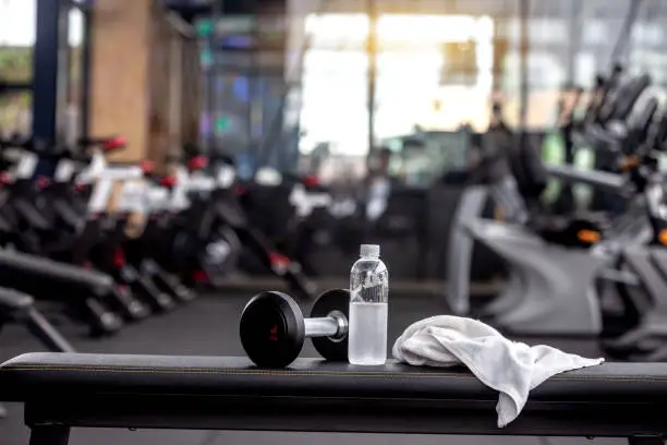 Dumbbell, water bottle, towel on the bench in the gym.
