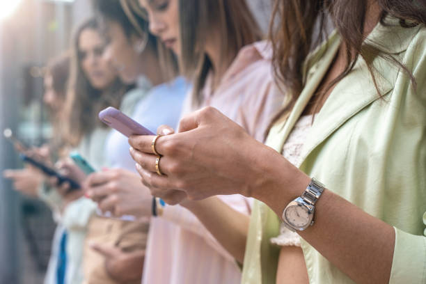 istock Group of interracial girls intensively using smartphone and social network application standing against a wall. Close up on the hands holding the cellphone. Youth and technology concept. 1322158201