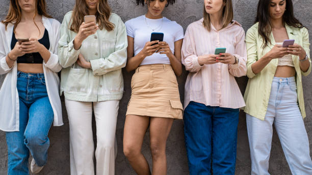 istock Generation z people using tech concept. Just girls standing against a wall browsing social media content from the smartphone screens. Mid section crop. 1322158202