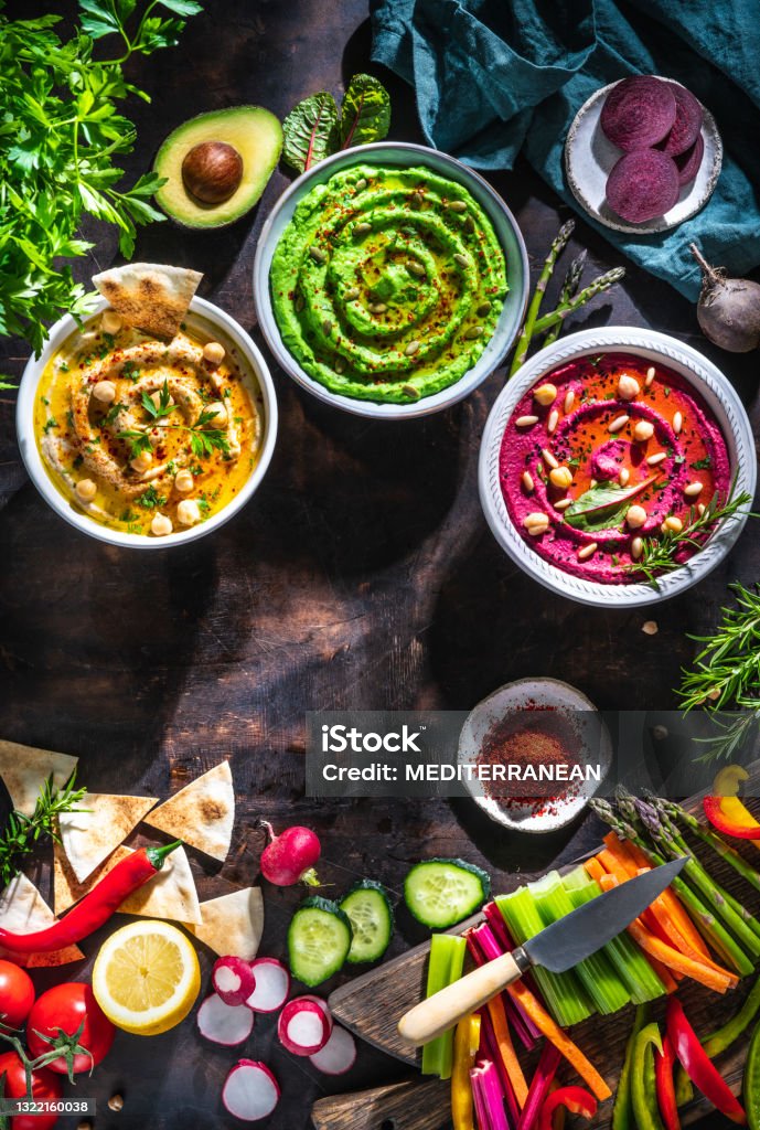 Hummus Three bowl of chickpeas, avocado and beetroot with cut vegetables sticks on dark wood table Hummus Three bowl of chickpeas, avocado and beetroot with cut vegetables for dip on dark wooden table background Vegan Food Stock Photo