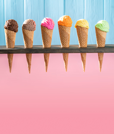 Assorted ice cream waffle cones in a row colorful different flavor as chocolate, mango, strawberry, mint, vanilla, lemon, coffee, nuts on pink and blue wooden wall