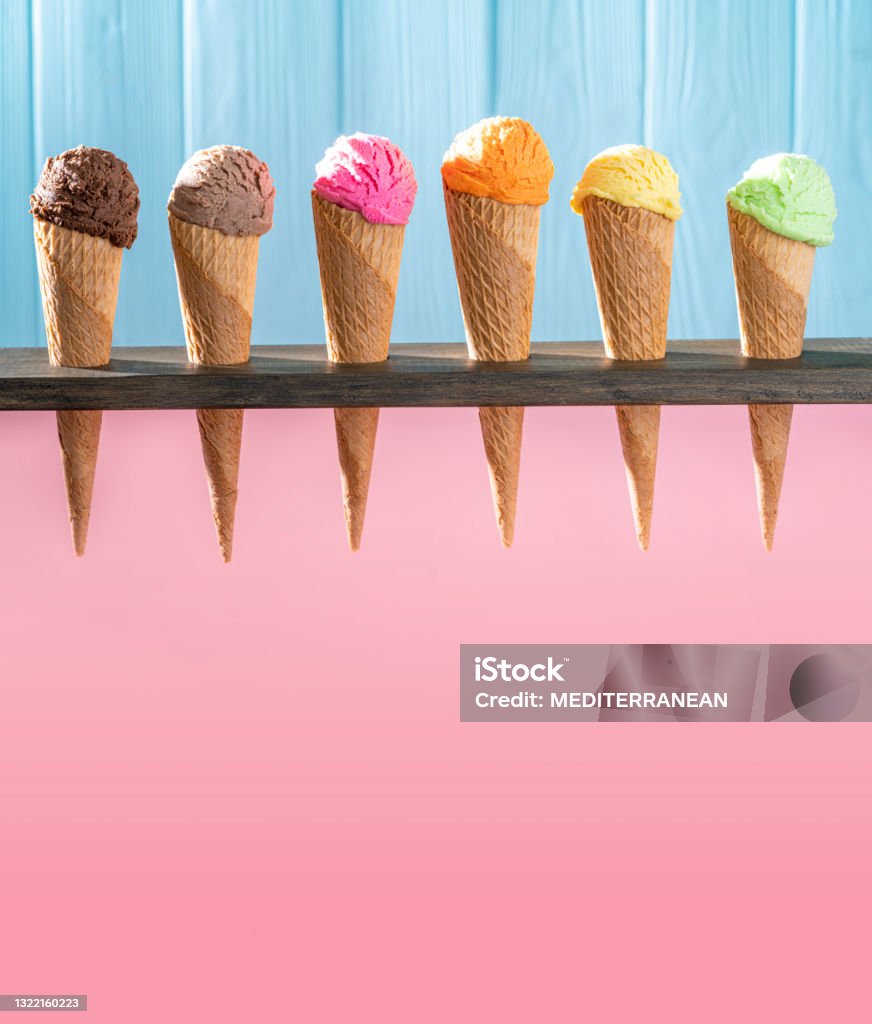 Assorted ice cream waffle cones in a row colorful different flavor on pink and blue wood Assorted ice cream waffle cones in a row colorful different flavor as chocolate, mango, strawberry, mint, vanilla, lemon, coffee, nuts on pink and blue wooden wall Ice Cream Stock Photo