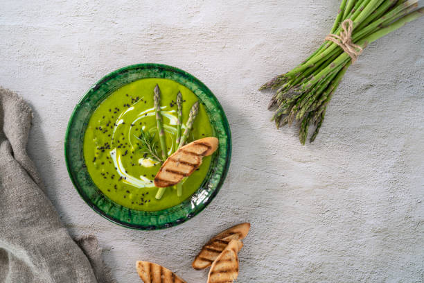 piatto zuppa di asparagi con ingredienti e pane tostato su cemento bianco - leaf vegetable asparagus green vegetable foto e immagini stock