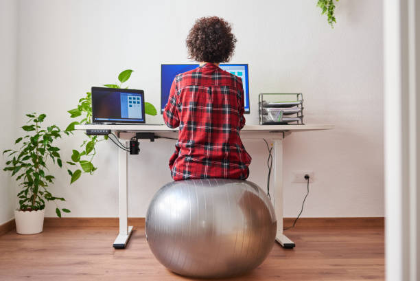 Woman teleworking sitting on a fitball Back view of a woman teleworking sitting on a fitball in front of her desk fitness ball stock pictures, royalty-free photos & images