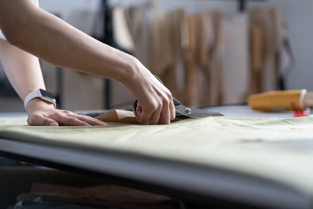 dressmaker hand verwenden schere geschnitten stoffmaterial zu nähen. nahaufnahme des arbeitsprozesses in schneiderwerkstatt - designer einrichtung fotos stock-fotos und bilder