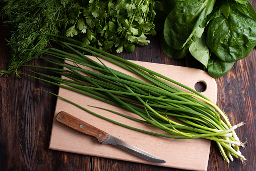 Bunch of fresh green onions with greens on a cutting board on a wooden background, rustic style, useful vegetarian food concept, close up.