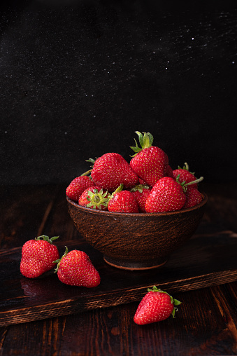 Fresh strawberries in a bowl on dark wooden background, summer concept, close up.