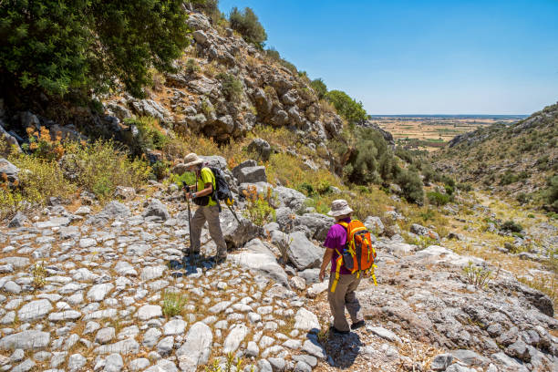 istock Elderly couple with backpacks trekking on ancient pavement path 1322170939