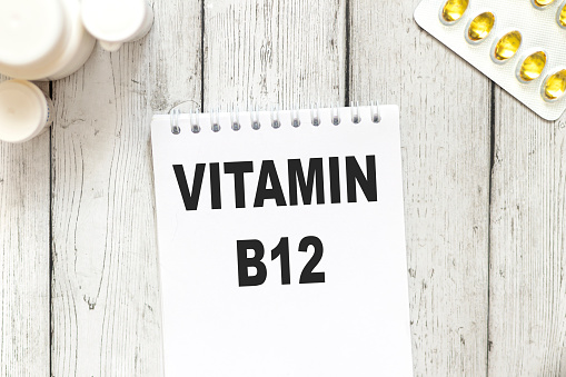 vitamin b12, text on white notepad paper on wooden table background near capsules and tablets