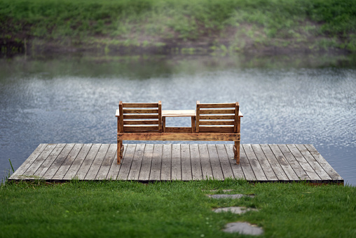 Wooden bench with table on river pier in morning mist on eco Irpin city embankment