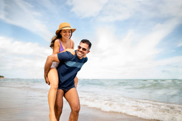 Smiling couple on the beach walking and enjoying the view Husband carrying his wife on his arms, walking on the beach male swimsuit standing arm around stock pictures, royalty-free photos & images