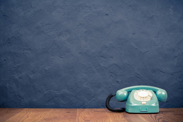 istock Retro rotary telephone on table front textured black concrete wall background. Vintage old style filtered photo 1322185587