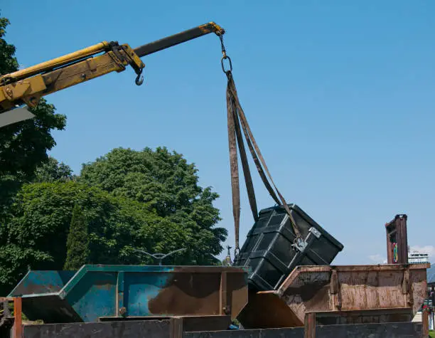 Photo of Loading garbage containers into a truck using a crane. Slinger works.